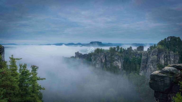 Nebliges Tal, die Basteibrücke im Elbsandsteingebirge zur blauen Stunde mit Nebel in den Tälern