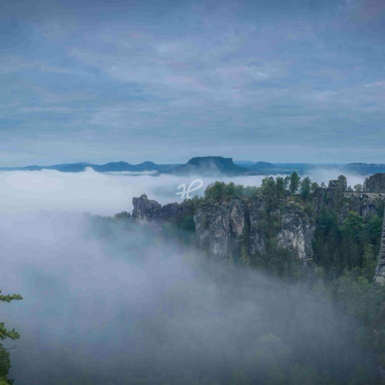 Nebliges Tal, die Basteibrücke im Elbsandsteingebirge zur blauen Stunde mit Nebel in den Tälern