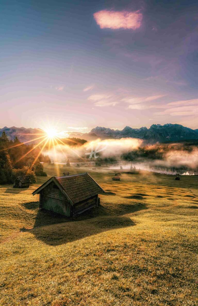 Sonnenaufgang am Geroldseein den bayerischen Alpen im Herbst ohne Wolken mit Sonnenstern im Hochformat