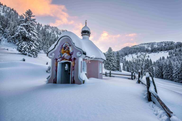 Eine Kapelle im Tiefschnee zum Sonnenuntergang im Oberammergau