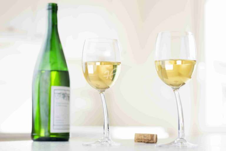 Zwei Gläser Weißwein, Riesling, mit grüner Weinflasche in einem hellen Raum
