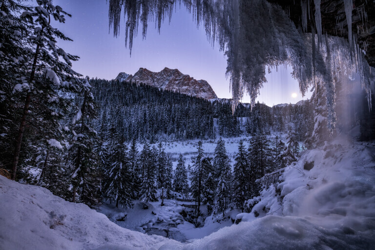 Wasserfall im Winter mit Eiszapfen und Bergen mit mondschein