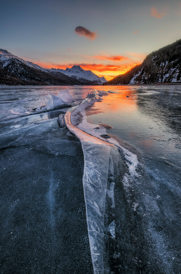 Gefrorener See in der Schweiz mit Eisstruktur und einem Riss zum Sonnenuntergang