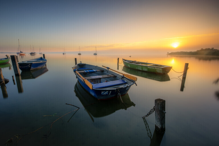 sonnenaufgang mit etwas Nebel und Booten am See