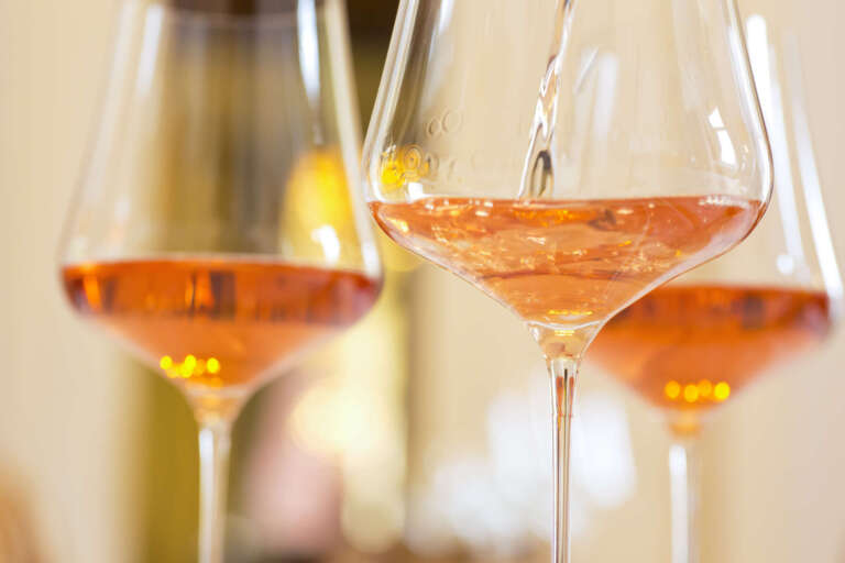 Roséwein wir in ein Glas eingeschenkt vor festlichem Hintergrund