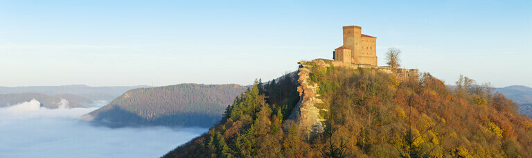 Die Burg Trifels bei Sonnenaufgang im Herbst mit Nebel im Tal